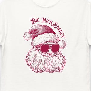 May include: A white t-shirt with a red illustration of Santa Claus wearing sunglasses. The text "Big Nick Energy" is above Santa's head.