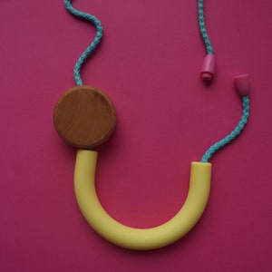 May include: A wooden circle attached to a yellow rubber loop and a turquoise rope with pink plastic ends. The rope is looped around the wooden circle and the rubber loop.