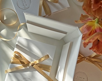 May include: White envelopes with gold ribbon and a round logo that says "Yari M. Photography" in cursive. The envelopes are stacked on top of each other.