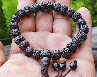 May include: A brown wooden mala bracelet with a dark brown tassel. The beads are round and have a textured surface.