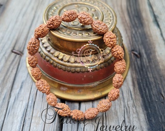 May include: A brown wooden bracelet made of small, round beads. The bracelet is resting on a gold and red decorative stand.