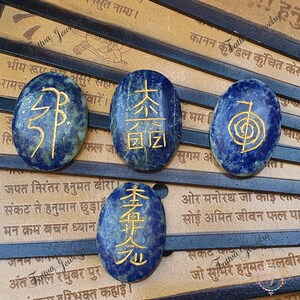 May include: Four oval-shaped lapis lazuli stones with gold lettering. The stones are arranged in a row on a brown surface. The stones feature different symbols and characters, including the Chinese characters for "Tai Shi Li Sheng Yuan" and a symbol that resembles a spiral.