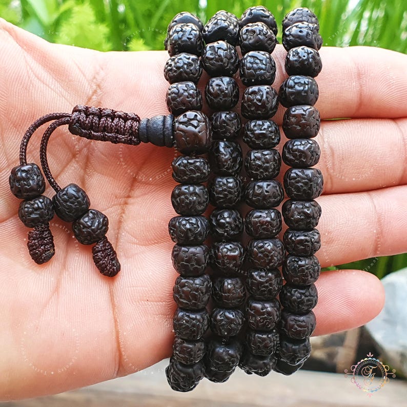 May include: A black mala bead necklace with a tassel. The beads are made of wood and have a rough texture.