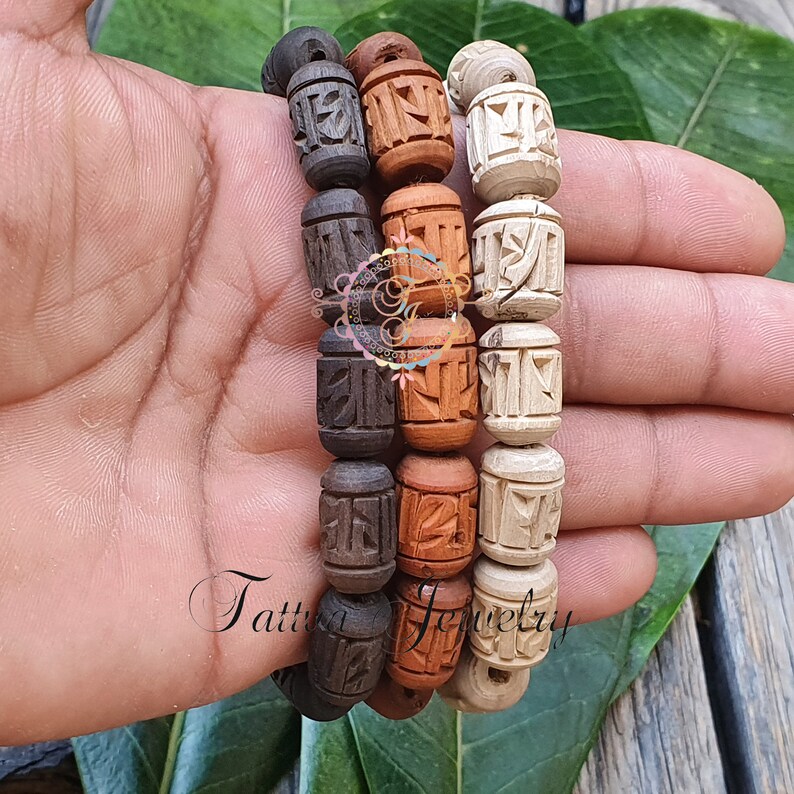 Pode incluir: Tr&ecirc;s pulseiras de madeira com entalhes intrincados. As pulseiras s&atilde;o de cor marrom, laranja e branco. As pulseiras est&atilde;o empilhadas umas sobre as outras.