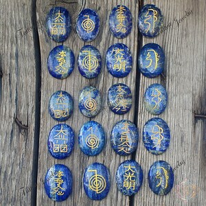 May include: Set of 16 oval-shaped lapis lazuli stones with gold symbols and characters. The stones are arranged in four rows of four.