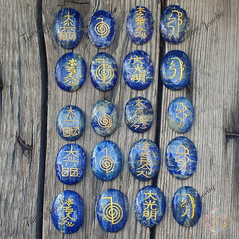 May include: Set of 16 oval-shaped lapis lazuli stones with gold symbols and characters. The stones are arranged in four rows of four.