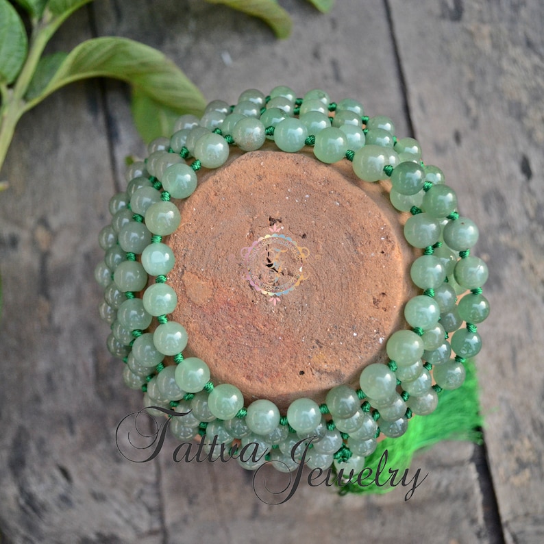 May include: A green jade mala necklace with a tassel. The necklace is made of round beads and is strung on a green cord.