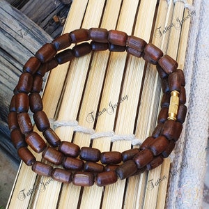 May include: A brown wooden beaded necklace with a gold clasp. The necklace is made of multiple strands of beads and is lying on a woven bamboo surface.