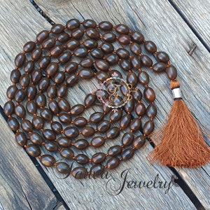 May include: A brown mala necklace with a tassel made of brown string. The necklace is made of oval-shaped beads.