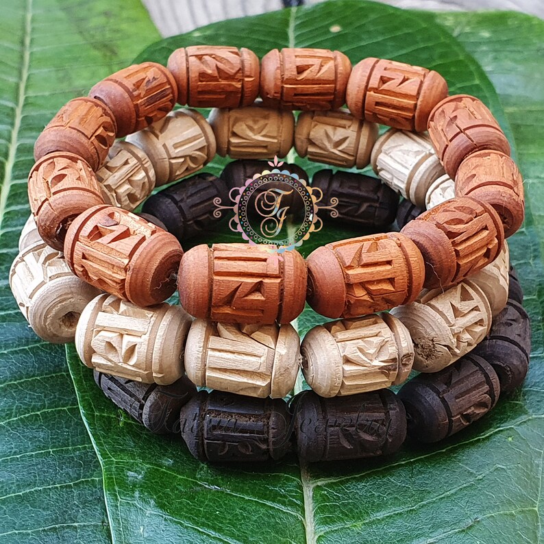 Pode incluir: Tr&ecirc;s pulseiras de madeira com entalhes intrincados. As pulseiras s&atilde;o feitas de madeira marrom escura, marrom clara e madeira natural. As pulseiras est&atilde;o empilhadas uma em cima da outra.