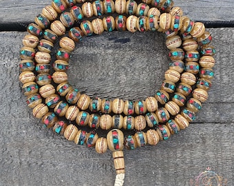 Puede incluir: Un collar de cuentas de oración con cuentas de madera de color marrón claro. Cada cuenta está decorada con detalles turquesa y rojos. Las cuentas están ensartadas y tienen una borla en el extremo. Las cuentas están dispuestas en un patrón circular.