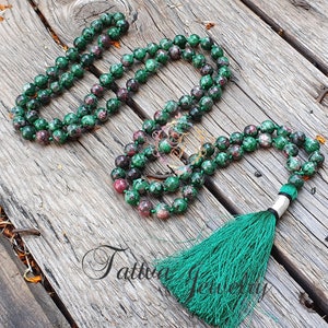 Puede incluir: Un collar mala de piedras preciosas verde y rosa con un borla verde. El collar está hecho de cuentas redondas y tiene aproximadamente 108 cuentas.