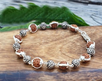 May include: A brown and silver bracelet with round beads. The beads are made of wood and have a silver Om symbol on them.
