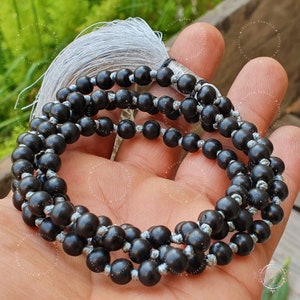 May include: A black wooden mala with a gray tassel. The mala is made of round beads and is strung on a gray cord.