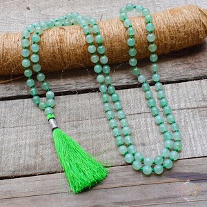 May include: A green jade mala bead necklace with a green tassel. The necklace is made of 108 beads and is strung on a thin cord.