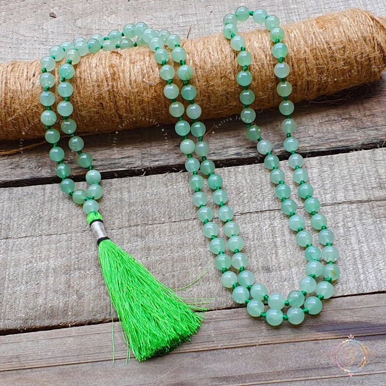 May include: A green jade mala bead necklace with a green tassel. The necklace is made of 108 beads and is strung on a thin cord.
