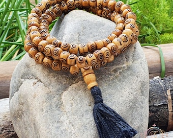 May include: A wooden mala bead necklace with a black tassel. The beads are brown and have a circular pattern carved into them.