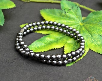 May include: A double-strand bracelet made of black hematite beads. The bracelet is lying on a green leaf.