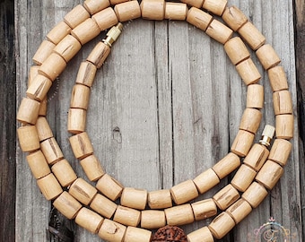 May include: A wooden mala necklace with a brown rudraksha bead at the end. The necklace is made of natural wood beads and has a gold-colored metal clasp.
