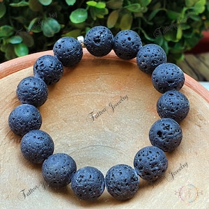 Könnte beinhalten: Ein schwarzes Armband aus Lava-Perlen mit einem silbernen Verschluss. Das Armband besteht aus runden Perlen mit einer rauen, strukturierten Oberfläche.