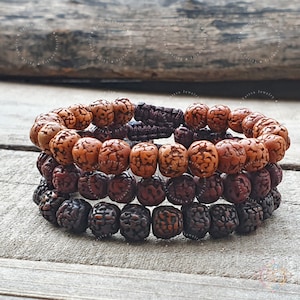 May include: Three stacked bracelets made of brown and black wooden beads. The beads are round and have a textured surface. The bracelets are tied together with a brown cord.