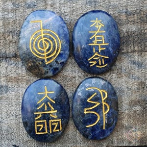 Puede incluir: Cuatro piedras lisas de lapisl&aacute;zuli azul ovaladas con s&iacute;mbolos dorados grabados en la superficie. Los s&iacute;mbolos son "木 (madera)", "火 (fuego)", "土 (tierra)" y "金 (metal)".