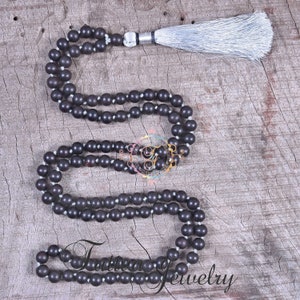 May include: A dark brown wooden mala necklace with a silver tassel. The necklace is made of round beads and is strung on a thin cord.