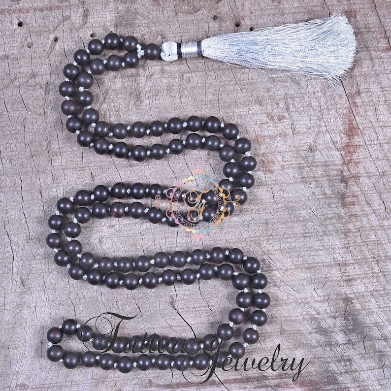 May include: A dark brown wooden mala necklace with a silver tassel. The necklace is made of round beads and is strung on a thin cord.