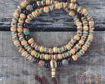 Puede incluir: Un collar de capas de cuentas de madera con detalles turquesa y rojos. El collar tiene una borla y un colgante decorativo. Las cuentas son de color beige claro y el collar se exhibe sobre una superficie de madera.