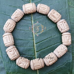 Pode incluir: Um bracelete de madeira com contas esculpidas. As contas s&atilde;o de cor castanho claro e t&ecirc;m desenhos intrincados. O bracelete est&aacute; sobre um fundo de folha verde.