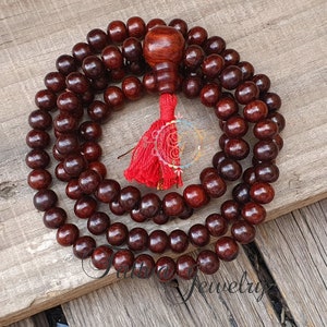 May include: A dark brown wooden mala bead necklace with a red tassel. The beads are round and smooth, and the tassel is made of a soft, silky material.