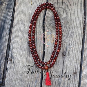 May include: A dark red wooden mala bead necklace with a red tassel. The necklace is made of round beads and is approximately 108 beads long.