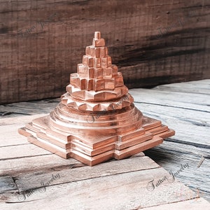 Könnte beinhalten: Eine pyramidenförmige Skulptur aus Kupfer mit quadratischer Basis. Die Skulptur besteht aus mehreren Schichten und hat ein detailliertes Design.