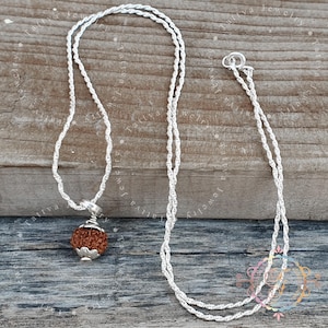 May include: A silver necklace with a twisted rope chain and a pendant. The pendant has a brown, textured bead with a silver cap. The necklace is displayed on a wooden surface.