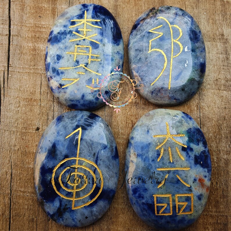 Puede incluir: Cuatro piedras lisas de forma ovalada de color azul con s&iacute;mbolos y caracteres dorados. Las piedras est&aacute;n dispuestas en forma de cuadrado sobre una superficie de madera. Los s&iacute;mbolos incluyen los caracteres chinos para "amor", "paz", "alegr&iacute;a" y "prosperidad".