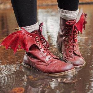 May include: Red leather boots with red wings attached to the ankles. The boots are standing in a puddle of water.
