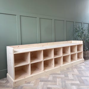 May include: A large, unfinished wooden storage unit with multiple cubby shelves. The unit is made of light-coloured wood and has a flat top. The design is simple and functional, suitable for various storage needs.