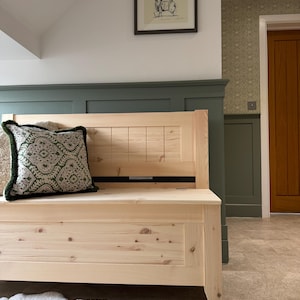 May include: A natural wood bench with a back and a seat. A patterned green and white cushion sits on the bench. A framed picture is on the wall above the bench. The bench is 120 cm long.