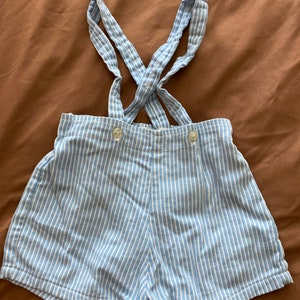 May include: Blue and white striped shorts with suspenders. The shorts have a button closure and are made of a lightweight fabric.