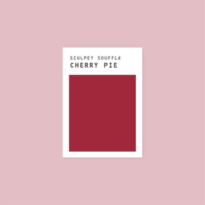 Puede incluir: Un cuadrado de arcilla para modelar Sculpey Souffle de color rojo, etiquetado como "Cherry Pie".