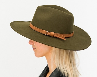 May include: A green felt fedora hat with a brown leather band and buckle. The hat has a wide brim and a slightly indented crown.