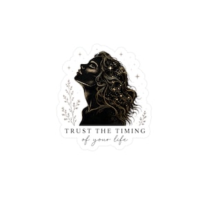 Op de afbeelding: Een sticker met een silhouet van een vrouw die omhoog kijkt, met sterren in haar haar. De tekst "TRUST THE TIMING of your life" staat eronder. Het ontwerp heeft een hemels en inspirerend thema.