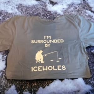 Peut inclure: Un t-shirt vert avec le texte "I'm surrounded by iceholes" et une silhouette d'une personne pêchant sur glace.