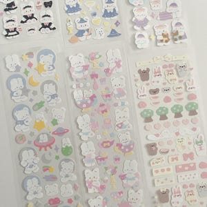 May include: A set of six sheets of stickers featuring cute cartoon bunnies in various poses and outfits. The stickers are on a clear background and are perfect for adding a touch of whimsy to planners, journals, and other craft projects.