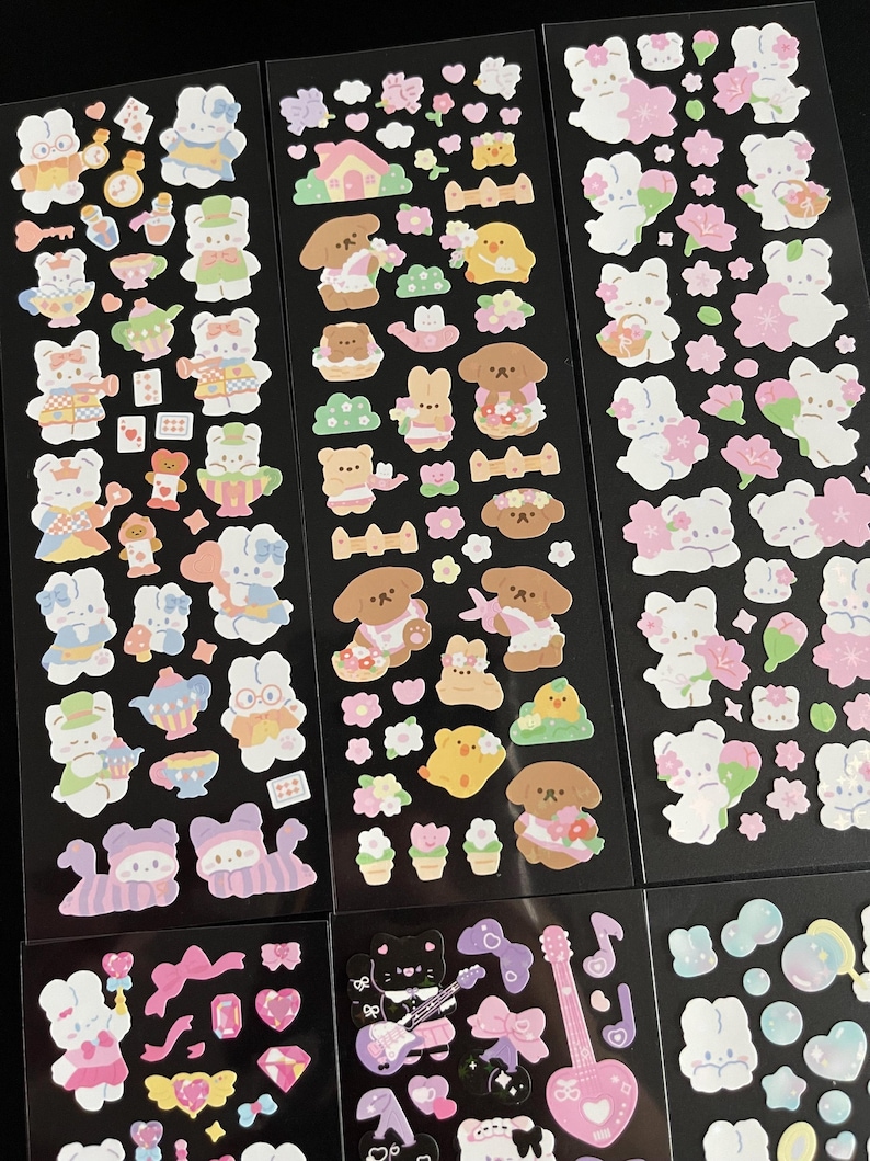 May include: A sheet of colorful stickers featuring cute cartoon characters, including bunnies, dogs, and cats. The stickers are arranged in rows on a black background. Some stickers have a floral theme, while others have a more whimsical design.