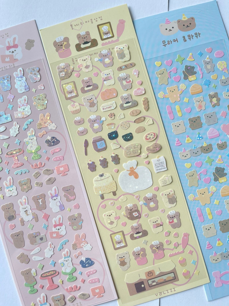 Puede incluir: Tres hojas de pegatinas con ositos de dibujos animados adorables en varias poses y actividades. Las pegatinas est&aacute;n sobre un fondo rosa claro, amarillo claro y azul claro. El texto en las pegatinas dice "무결점 곰팡" y "VOLZZZI".