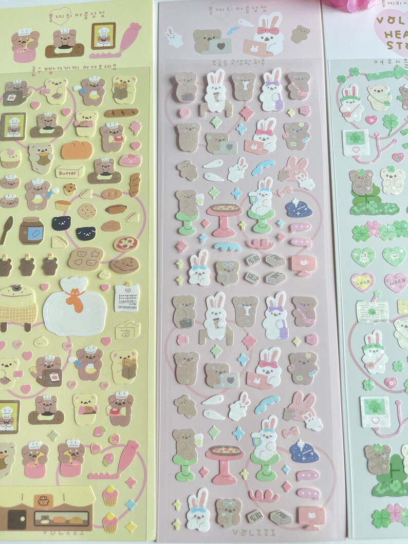Puede incluir: Tres hojas de pegatinas con osos y conejos de dibujos animados. Las pegatinas est&aacute;n sobre un fondo rosa y amarillo. La primera hoja presenta osos horneando, la segunda hoja presenta conejos con caf&eacute; y pizza, y la tercera hoja presenta conejos con corazones y tr&eacute;boles.