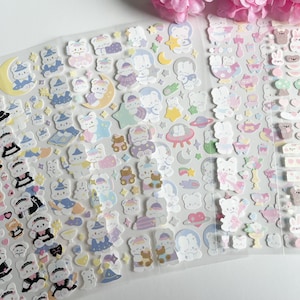 May include: A sheet of colorful stickers featuring cute cartoon bears in various poses and outfits. The stickers are on a clear background and are perfect for decorating planners, journals, and other items.