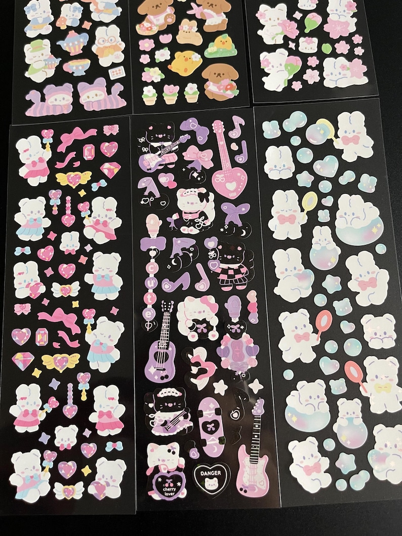 May include: A sheet of stickers featuring cute cartoon bears, hearts, stars, and other whimsical designs. The stickers are on a black background and are perfect for decorating journals, planners, laptops, and other items.
