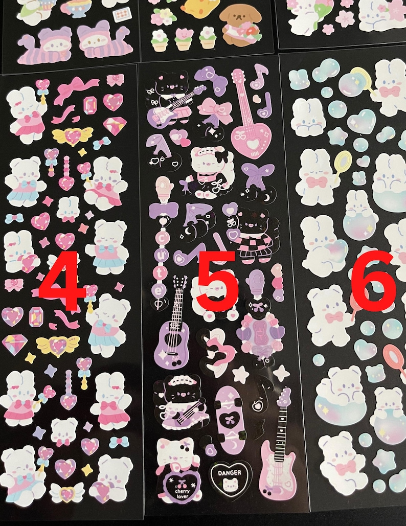 May include: Three sheets of stickers featuring cute cartoon characters. The stickers are on a black background and feature a variety of designs, including bunnies, hearts, stars, and musical instruments. The stickers are perfect for adding a touch of whimsy to your planner, journal, or laptop.
